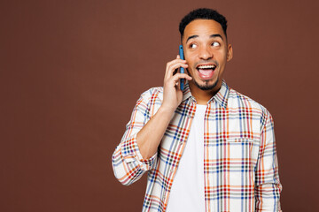 Wall Mural - Young smiling happy man of African American ethnicity he wear blue shirt casual clothes talk speak on mobile cell phone look aside isolated on plain brown background studio portrait Lifestyle concept