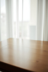Poster - A wooden table in a room with a blurred white curtain behind it, partially obstructing a view through a window._00001_