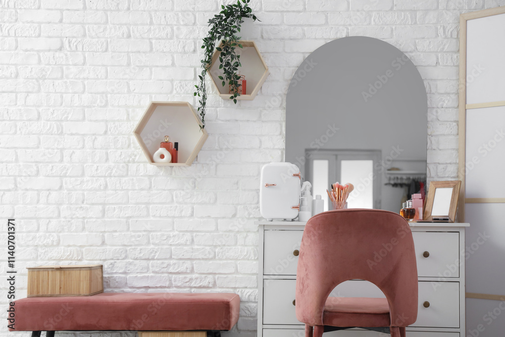 Dressing table with cosmetics, armchair and bench near light brick wall