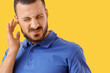 © Pixel-Shot - Young man suffering from ear pain on yellow background, closeup