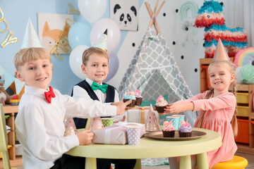 Wall Mural - Cute little happy kids with cupcakes and gift boxes celebrating birthday at table in children's room