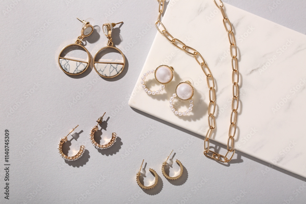 Board with different beautiful earrings and golden chain necklace on grey background