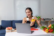 © Crystal - Asian nutritionist holding bell peppers and giving online consultation via laptop, promoting healthy eating habits