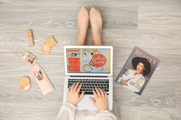 Wall Mural - Woman using laptop for online shopping and decorative cosmetics on light wooden floor