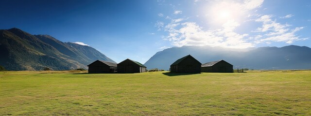 Aufkleber - A serene landscape featuring wooden structures against a backdrop of mountains and a bright sky.