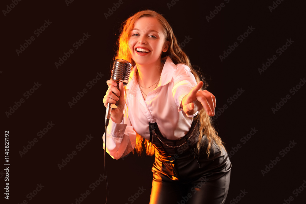 Beautiful young woman with microphone singing karaoke on black background
