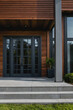 © MatandSterre - Modern home entrance with dark gray multi-paned French doors, stone steps, and a brown wood exterior.  Landscaping includes green ground cover.