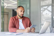 © Liubomir - A man holds a tablet while working at a desk with a laptop and notebook in a contemporary office space. He appears focused and immersed in his task.