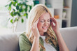© deagreez - Mature woman with blond hair sitting in living room feels headache while relaxing at home in casual green shirt