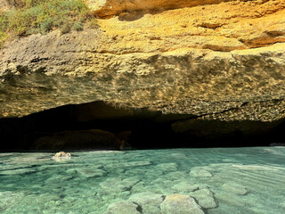 Poster - Cliff over blue sea water with stones at the bottom.