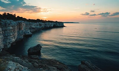 Wall Mural - Rocky coastline at sunset with swimmers.