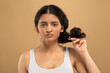 © Prostock-studio - A young Indian woman pulls her hair into a bun, focusing on her beauty routine. Seated against a neutral background, she embodies self-care and relaxation as part of her daily ritual.
