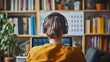 © aun - A person wearing headphones, focused on writing their goals in an app on a tablet, surrounded by books and a motivational calendar on the wall
