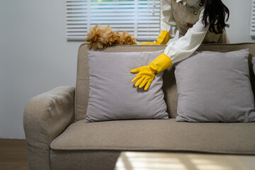 Housekeeper wearing yellow gloves diligently cleaning a sofa with a feather duster, creating a dust-free and inviting living room atmosphere for a comfortable home environment