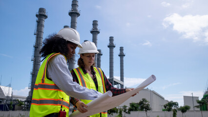 Wall Mural - Engineers wearing safety gear, including hard hats examining survey a large blueprint tablet standing industrial facility gas or oil refinery engaged in a job requires high safety standards concept.