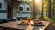 © Amir Bajric - Camping picnic, food and drink on wooden table in front of travel trailer in forest nature.