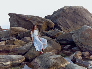 Poster - Serene woman in white dress relaxing on rocks at water's edge with feet in the water