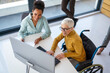 © NDABCREATIVITY - Disabled woman in wheelchair looking at computer, discussing startup project with interracial team
