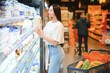 © Serhii - Young smiling happy woman 20s wear casual clothes shopping at supermaket store buy choose milk