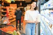 © Serhii - Young smiling happy woman 20s in casual clothes shopping at supermaket store with grocery cart