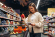 © standret - Shelves with products. Beautiful woman is in the supermarket