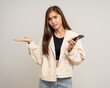 © Chanakon - Pretty young asian woman using smartphone feeling upset confused bad depressed emotional standing on isolated white background. Holding cell phone. Thinking and stressed