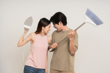 Wall Mural - Upset People quarreling unhappy asian couple attractive in various action gesture holding iron and broom on isolated white background. Stressed young man and woman clean house together