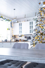 Wall Mural - Grey Wooden empty table to demonstrate product with space for text with upholstered chairs in white kitchen, modern interior with Christmas tree and fairy lights. New Year, Christmas mood, cozy home.