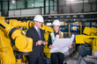 © FotoArtist - Professionals Discussing Plans in a Modern Industrial Facility With Robotic Machinery