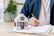 © Sumala - person signing documents with house model on desk