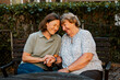 © Maskot - Smiling female nurse holding hand of senior woman while sitting on bench at park
