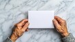 © Nattapun - An elderly person holds a blank card, conveying emotions of nostalgia and reflection on a marble table surface.