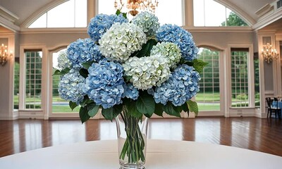 Canvas Print - A stunning arrangement of blue and white hydrangeas is displayed in a clear vase on a table in a bright and airy event space with large windows