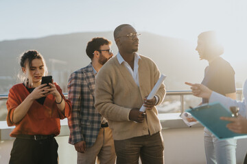 Wall Mural - A diverse group of business people celebrate a successful achievement, enjoying music and conversation on a high tower balcony during a stunning sunset.