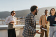 © qunica.com - A group of business colleagues dance and express joy on a high-rise balcony during sunset, celebrating success together with music and lively conversation.