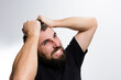 © Niko_Dali - A bearded man grips his hair tightly, his face contorted in a grimace of frustration and anger.  The image portrays stress, anxiety, and emotional distress against a plain background.