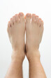 © Niko_Dali - Detailed view of two bare feet placed together, showcasing the toes, soles, and ankles against a clean white backdrop. The image emphasizes the skin texture and natural details of the feet.