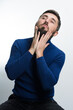 © Niko_Dali - A man with a beard, wearing a blue sweater and dark pants, gently touches his facial hair against a light background.