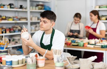 Wall Mural - Young man painting clay ceramic cup in workshop