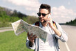 © Prostock-studio - Stressed male tourist with map standing on roadside, speaking on mobile phone, cannot catch car or find his travel route. Young man feeling lost while hitchhiking on highway, having problem