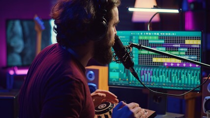 Fototapete - Music producer singing at home studio microphone to record songs, editing and adjusting volume levels in post production. Audio engineer conducts recordings of vocals, mixing console. Camera A.