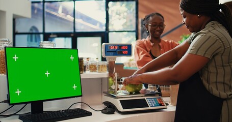 Seller serving customer at counter next to greenscreen layout, presenting blank copyspace template on monitor. Merchant using scale, having pc screen with isolated chromakey. Tripod shot.