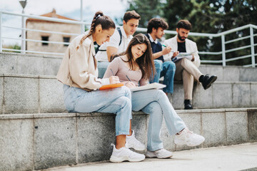 Poster - A group of university students collaborates in an outdoor setting with their professor offering guidance. They sit on steps, focusing on their notes and discussions in a supportive learning