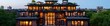 © AgungRikhi - Luxurious multi-story house with illuminated windows at dusk.