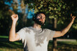 © qunica.com - A young man wearing headphones enjoys music outdoors. He appears relaxed and content under a bright, sunny sky in a lush green park. An expression of freedom and happiness is evident.