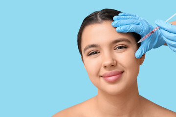 Sticker - Young woman receiving filler injection in face on blue background