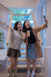 © Tj - Two asian female friends are taking a selfie with a smartphone while holding coffee inside a modern building, enjoying their time together and capturing memories