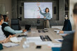 © qunica.com - A diverse group of business people gathered in a modern conference room for a meeting. A woman confidently presents data on a screen, engaging her colleagues in a focused discussion.