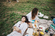 © qunica.com - A young couple relaxes on a picnic blanket, surrounded by food and painting supplies, enjoying a sunny day outdoors. The scene conveys creativity, leisure, and tranquility in a natural setting.