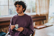 © qunica.com - A young man sits in a cozy cafe, holding a small coffee cup and looking contemplative. The relaxed ambiance and his thoughtful expression suggest a moment of reflection and leisure.